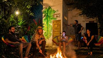 A group of people around a campfire at night, with a building in the background.