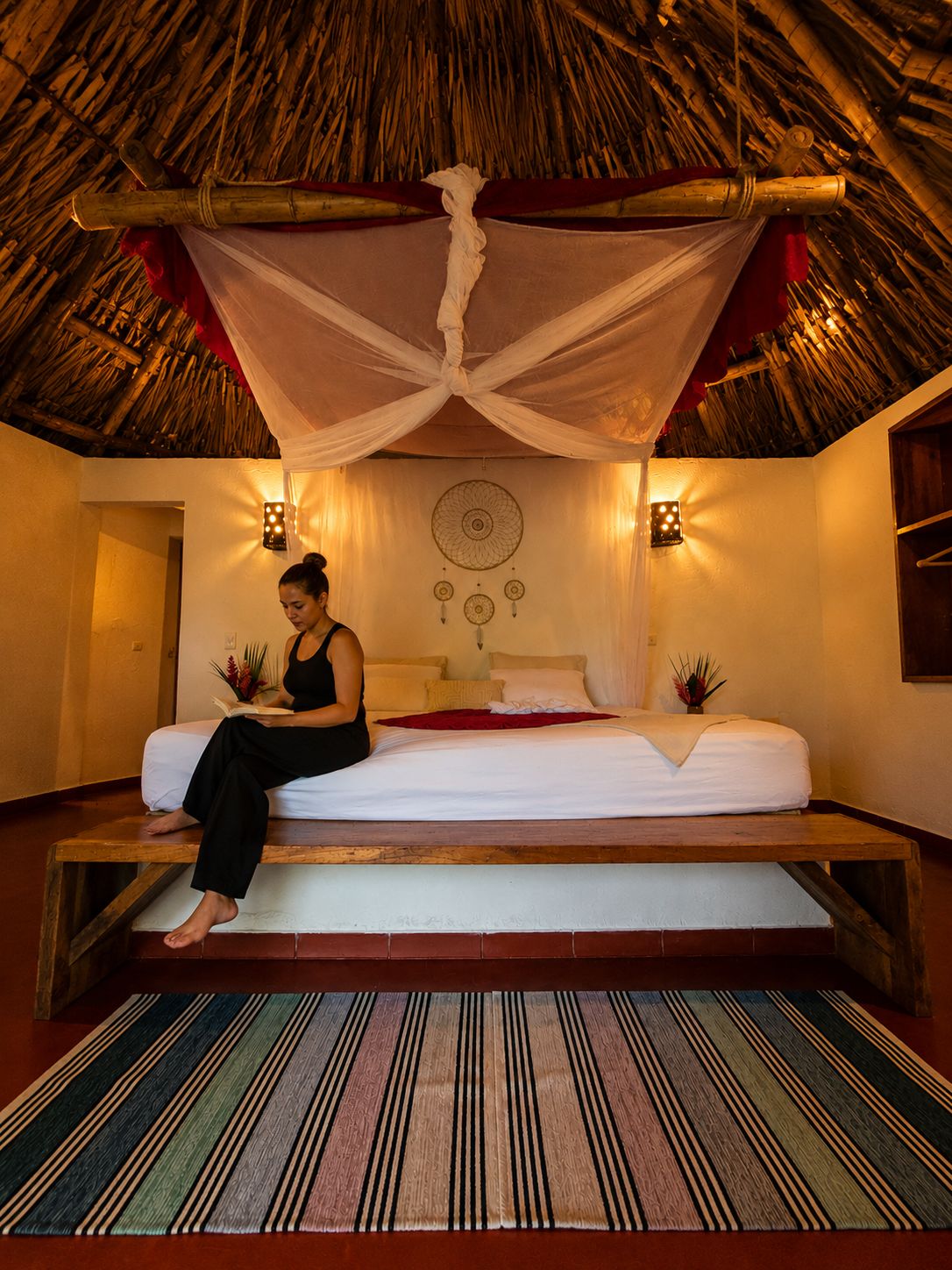 Una habitación con cama, un rincón de lectura y una pared decorativa con un atrapasueños.