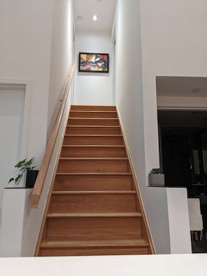 Un escalier en bois, doté d’une rampe, mène à un palier sur lequel est accrochée une œuvre d’art aux couleurs vives.