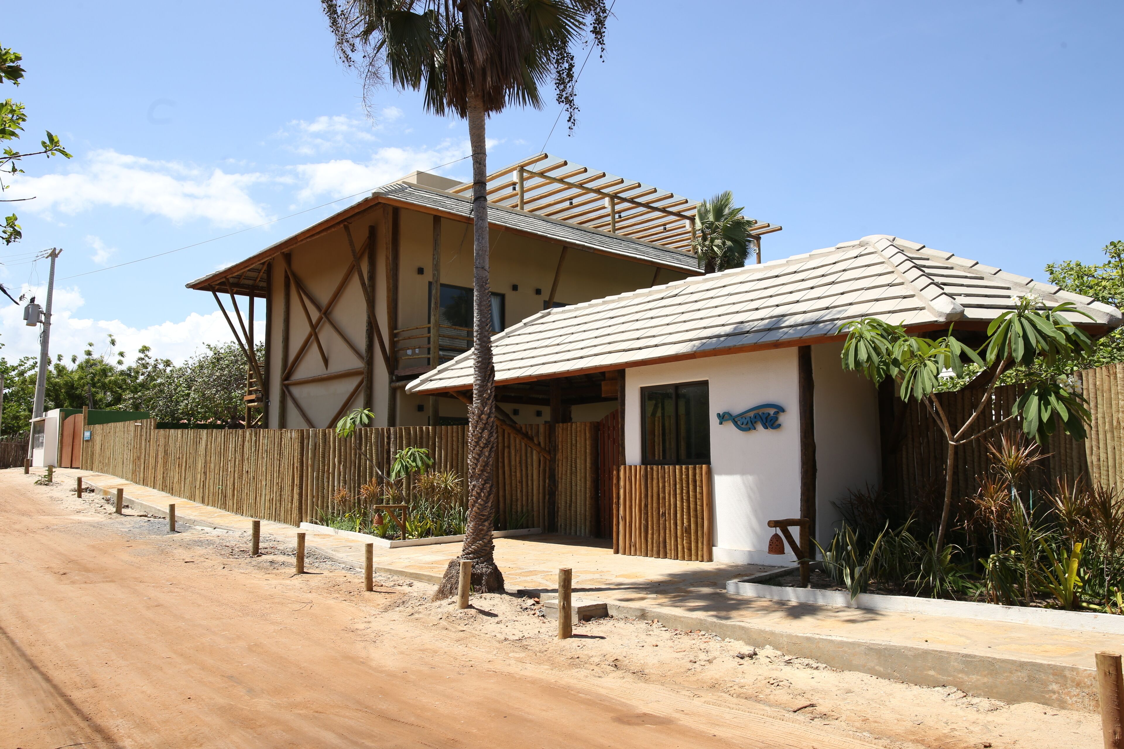 A two-story building with a wooden fence, a paved driveway, and tropical plants.