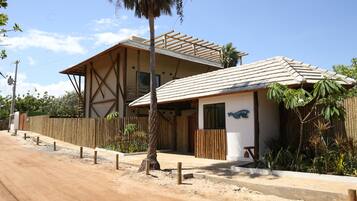 A two-story building with a wooden fence, a paved driveway, and tropical plants.