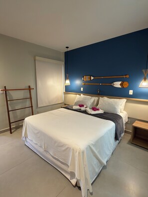 A neatly made bed with white linens and a gray blanket, a wooden ladder against the wall, and two wall-mounted lamps.