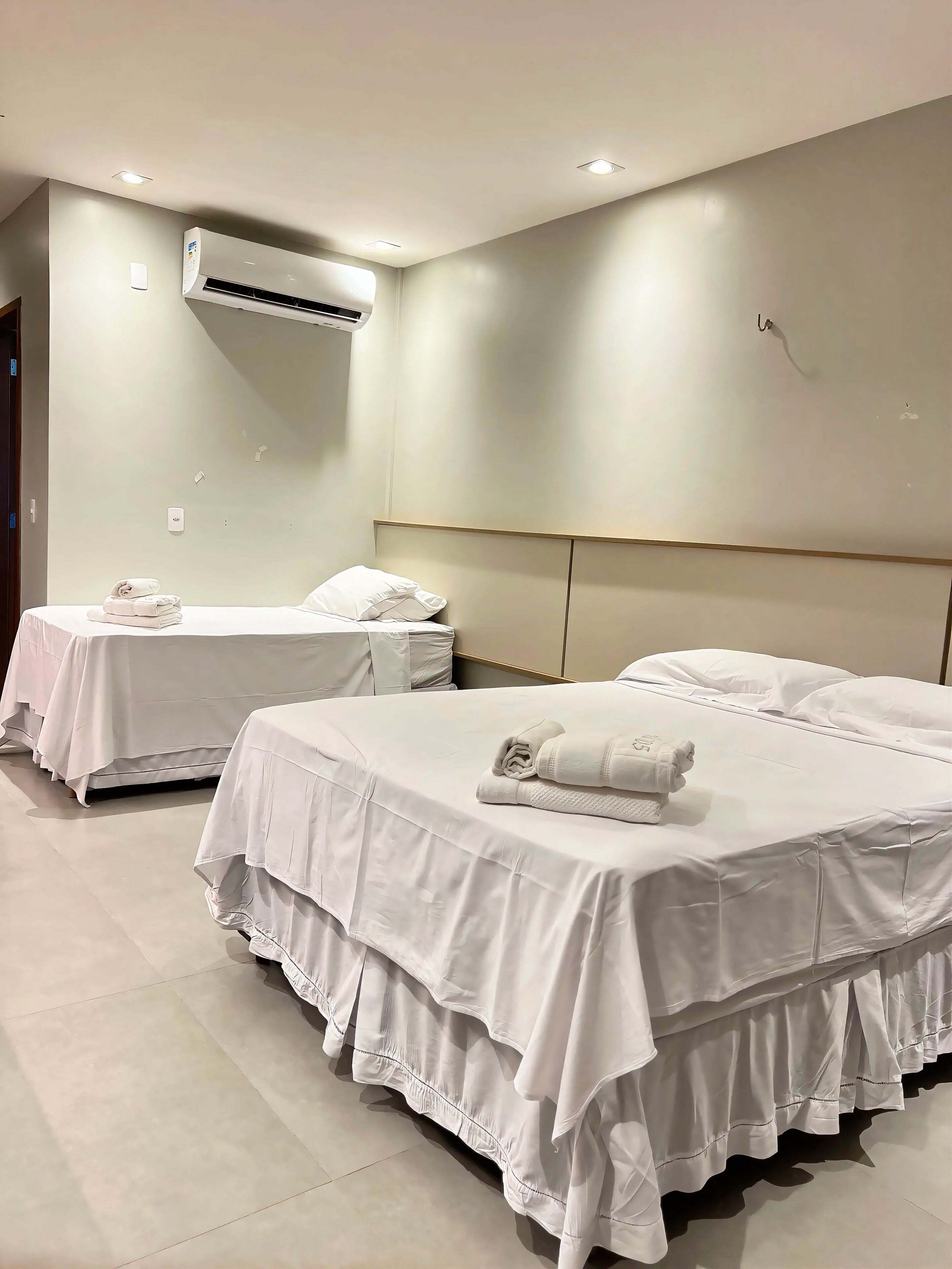Habitación de hotel con dos camas, cada una con cubrecama y almohadas blancas, y un equipo de aire acondicionado instalado en el techo.