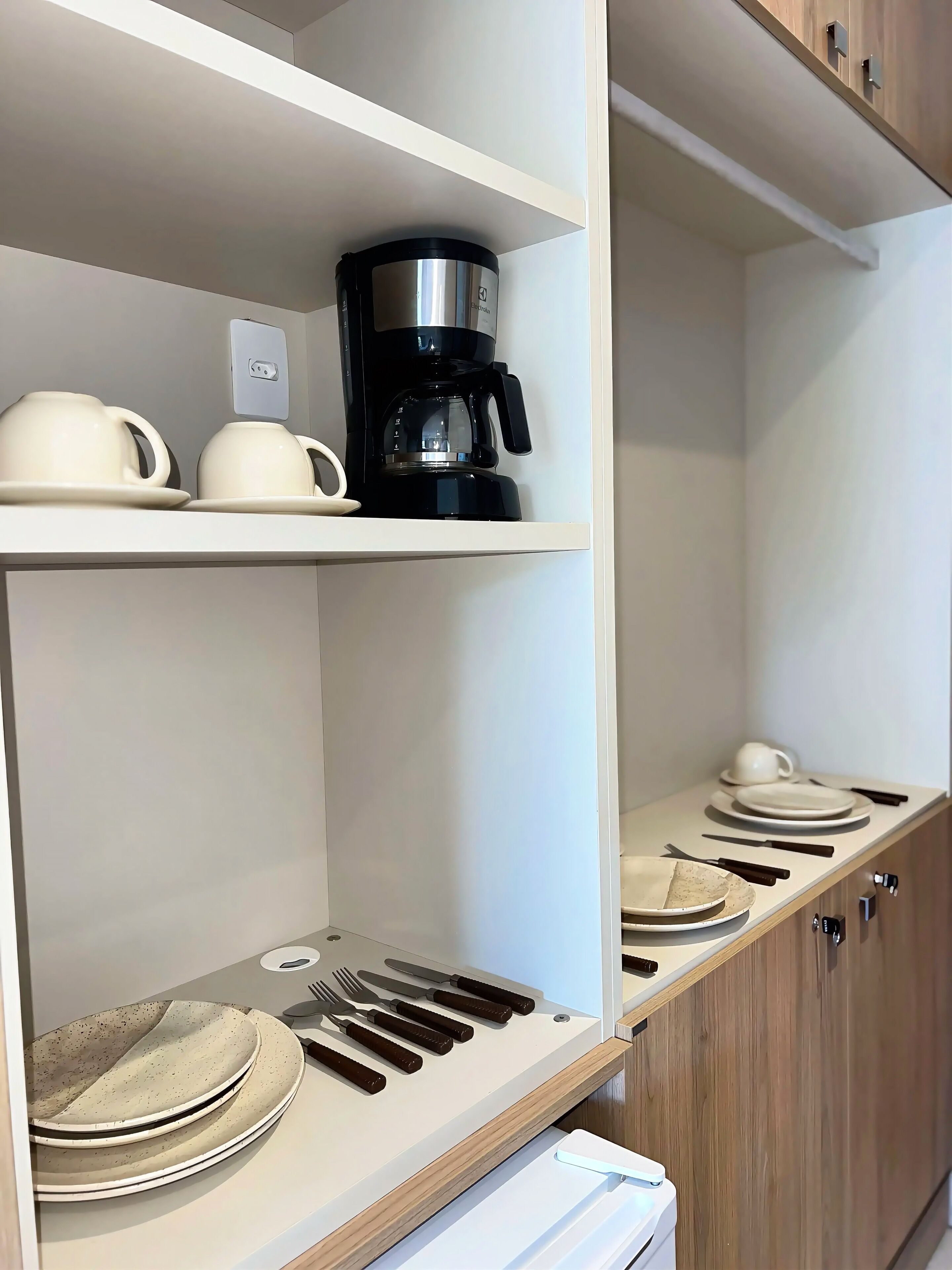 Una cocina con gabinetes blancos, una cafetera y utensilios y platos ordenados.