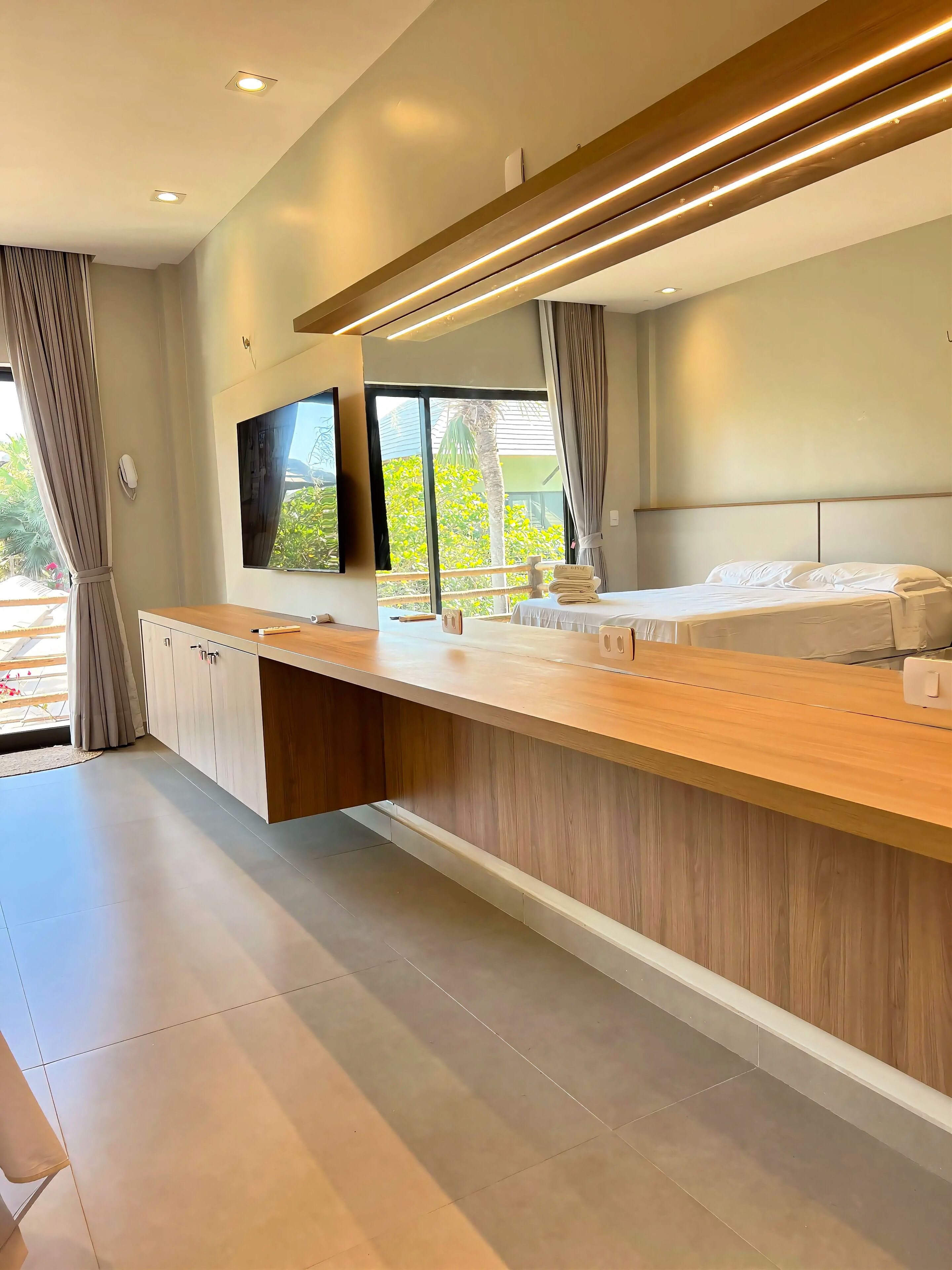 A modern hotel room with a large bed, a wooden desk, and a large window.