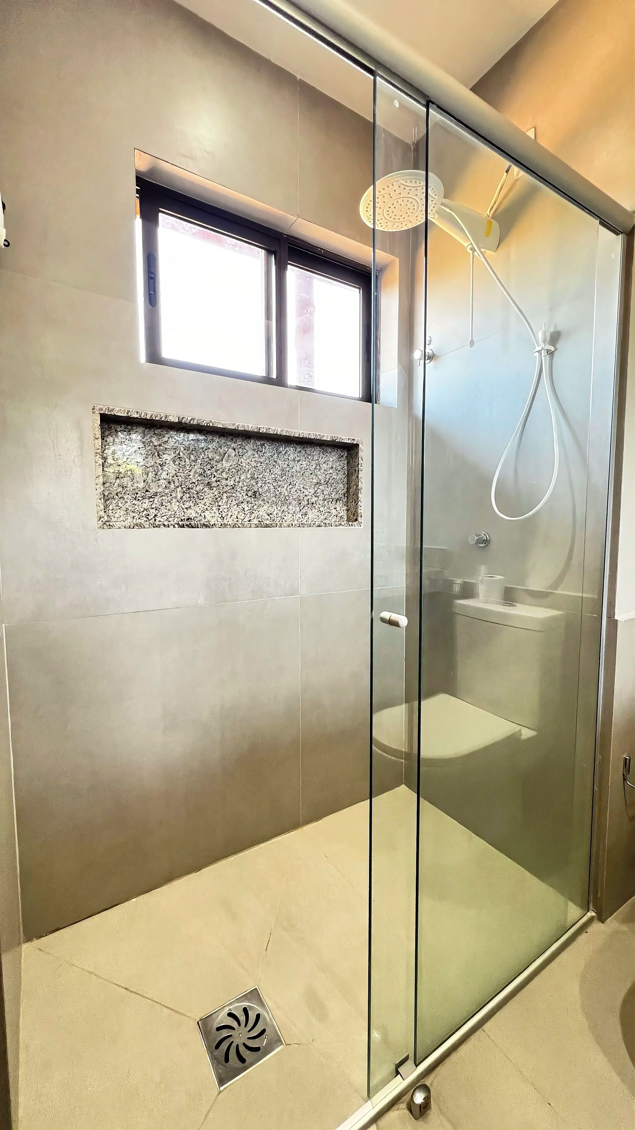 A modern bathroom with a glass shower enclosure, a built-in sink, and a window above the shower.