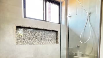A modern bathroom with a glass shower enclosure, a built-in sink, and a window above the shower.