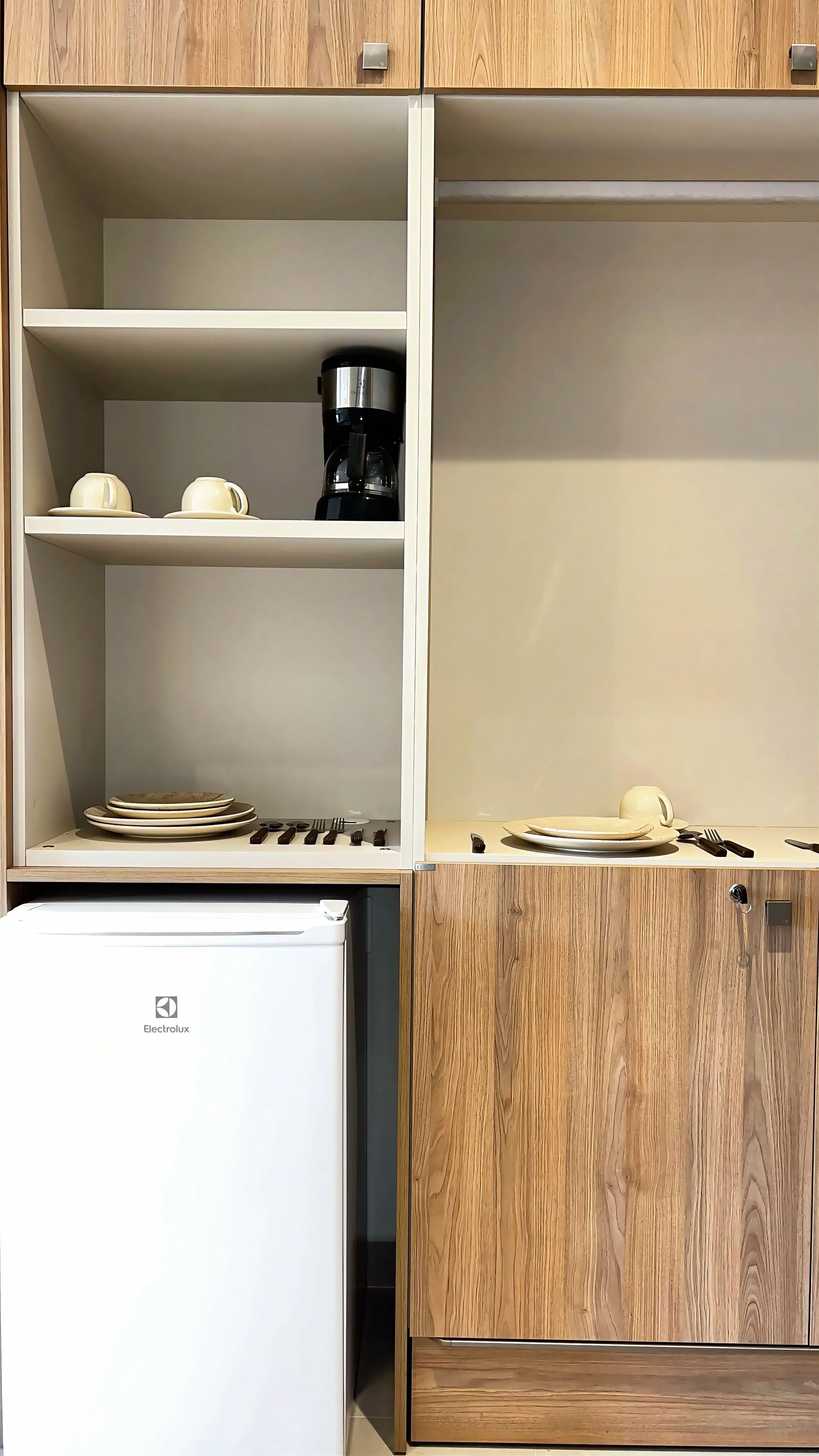 A compact kitchenette with a white refrigerator, wooden cabinets, and a coffee maker on the shelf.