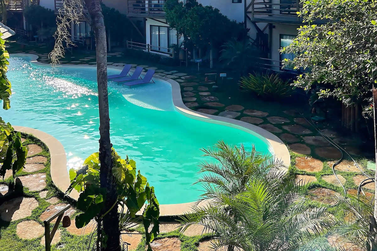 A resort with a swimming pool, palm trees, and a building with a balcony.
