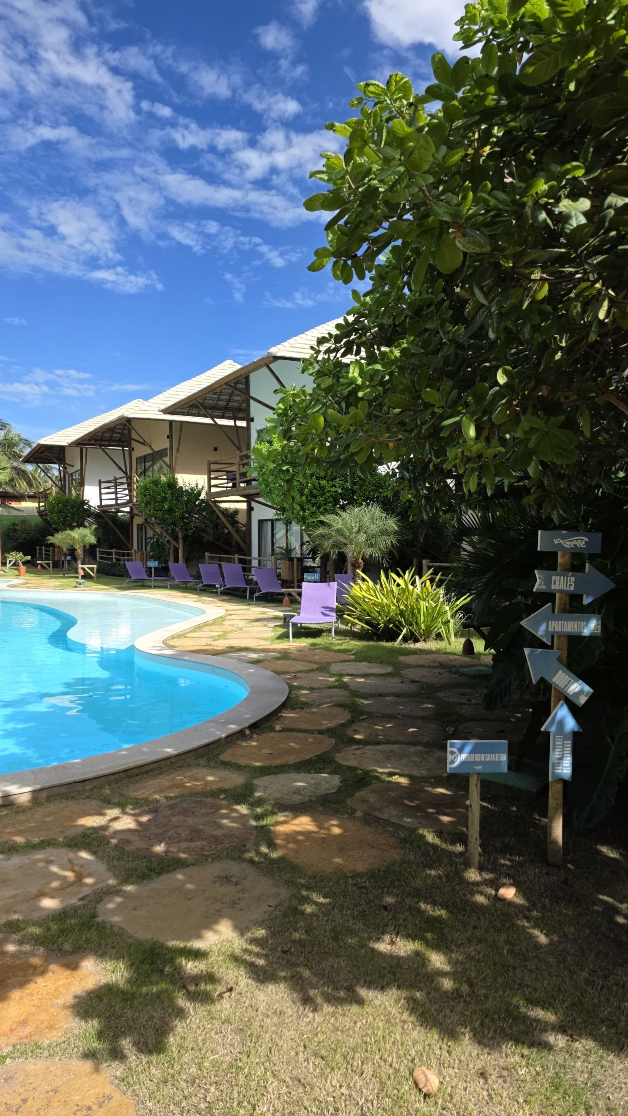 A pool area with lounge chairs, a signpost with directions, and a building with a sloped roof.