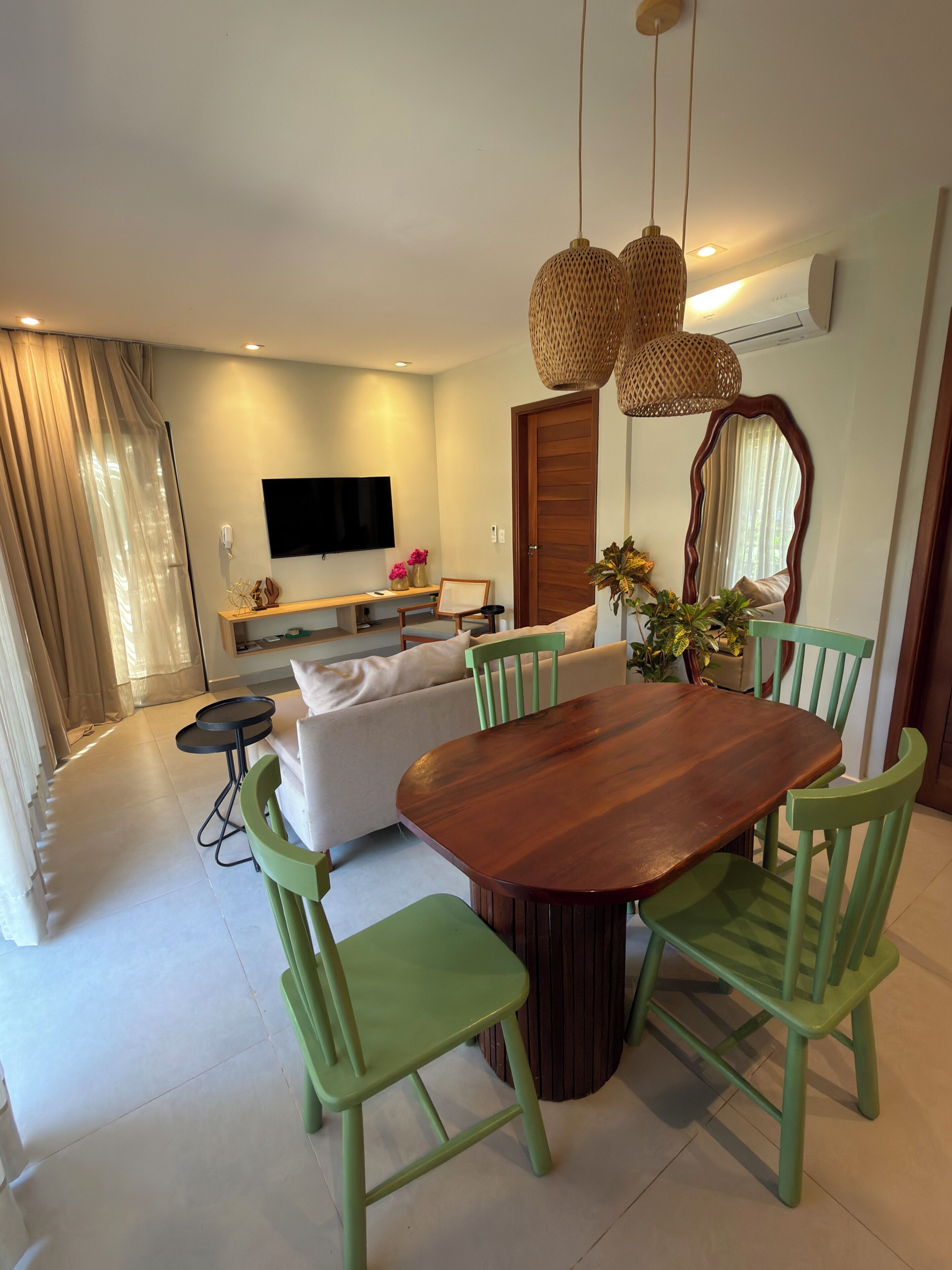Un salon moderne avec une table à manger en bois, des chaises vertes, un canapé, un téléviseur à écran plat et un grand miroir.