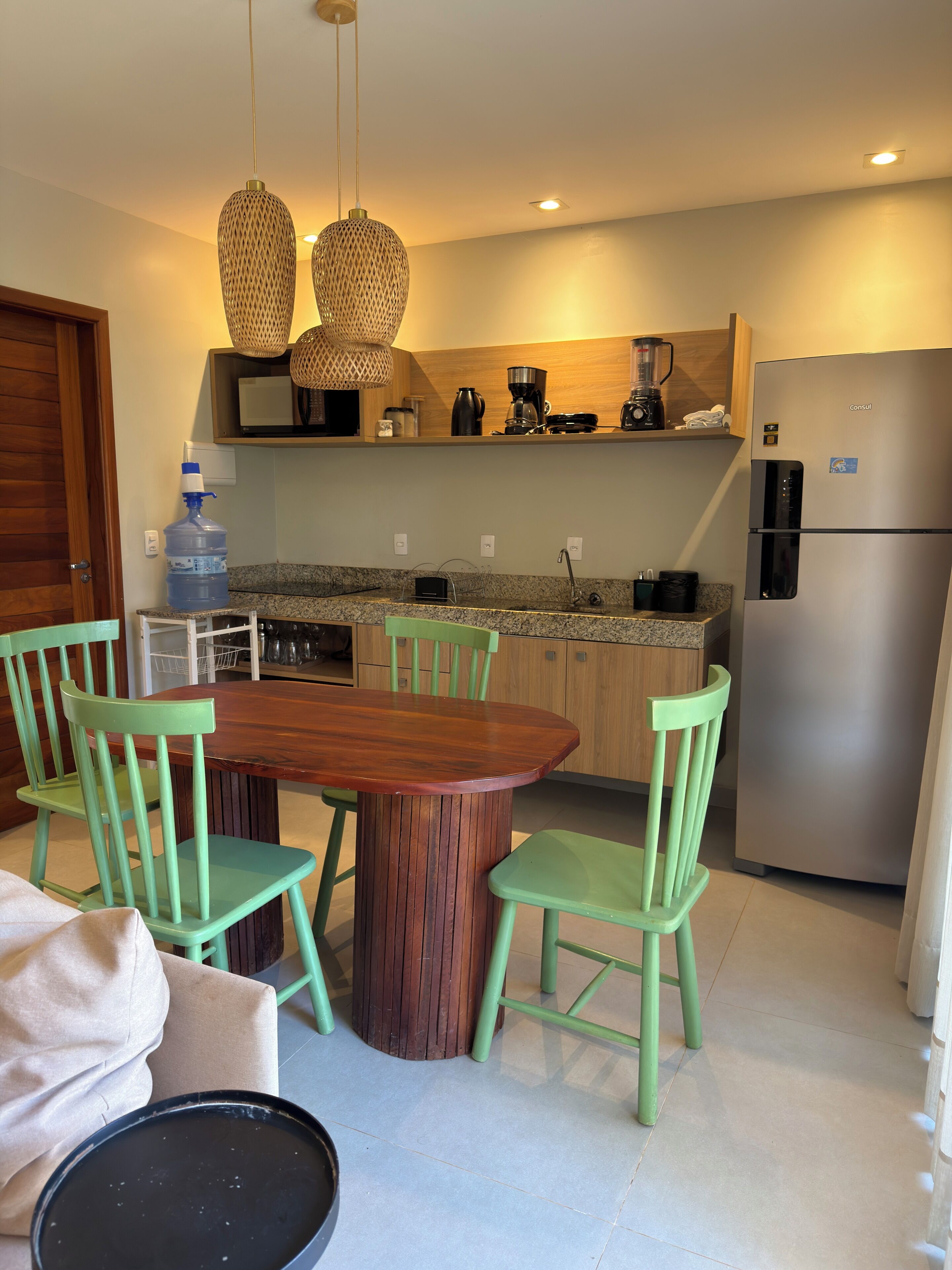 Una cocina moderna con una mesa de comedor de madera, sillas verdes, un refrigerador de acero inoxidable y lámparas colgantes.