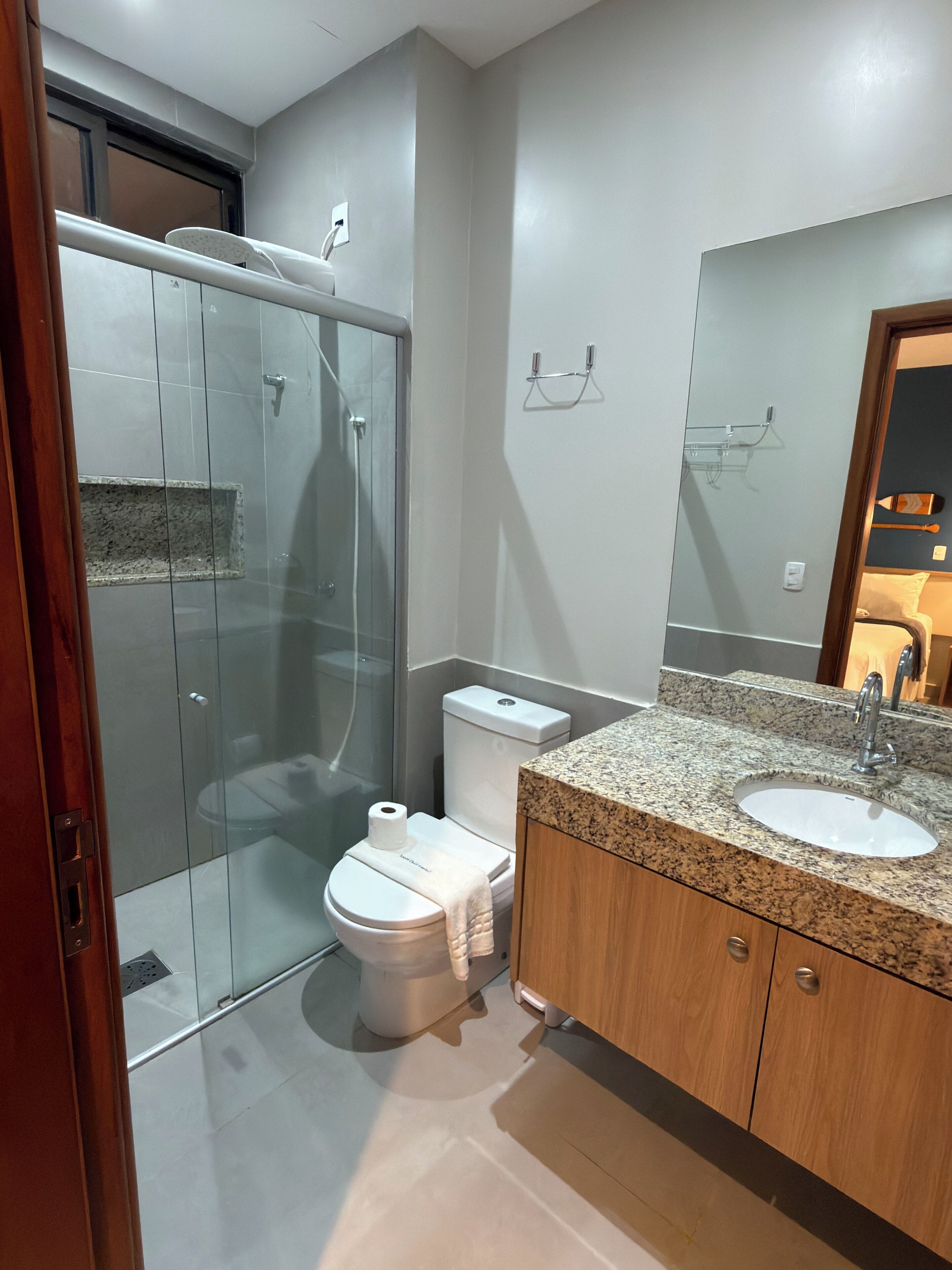 Uma casa de banho moderna com cabine de duche em vidro, sanita, lavatório com bancada de granito e espelho.