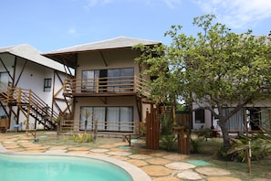 A two-story building with a balcony, a pool, and a garden area with various plants. - Condomínio Amaré (Cajueiro da Praia)