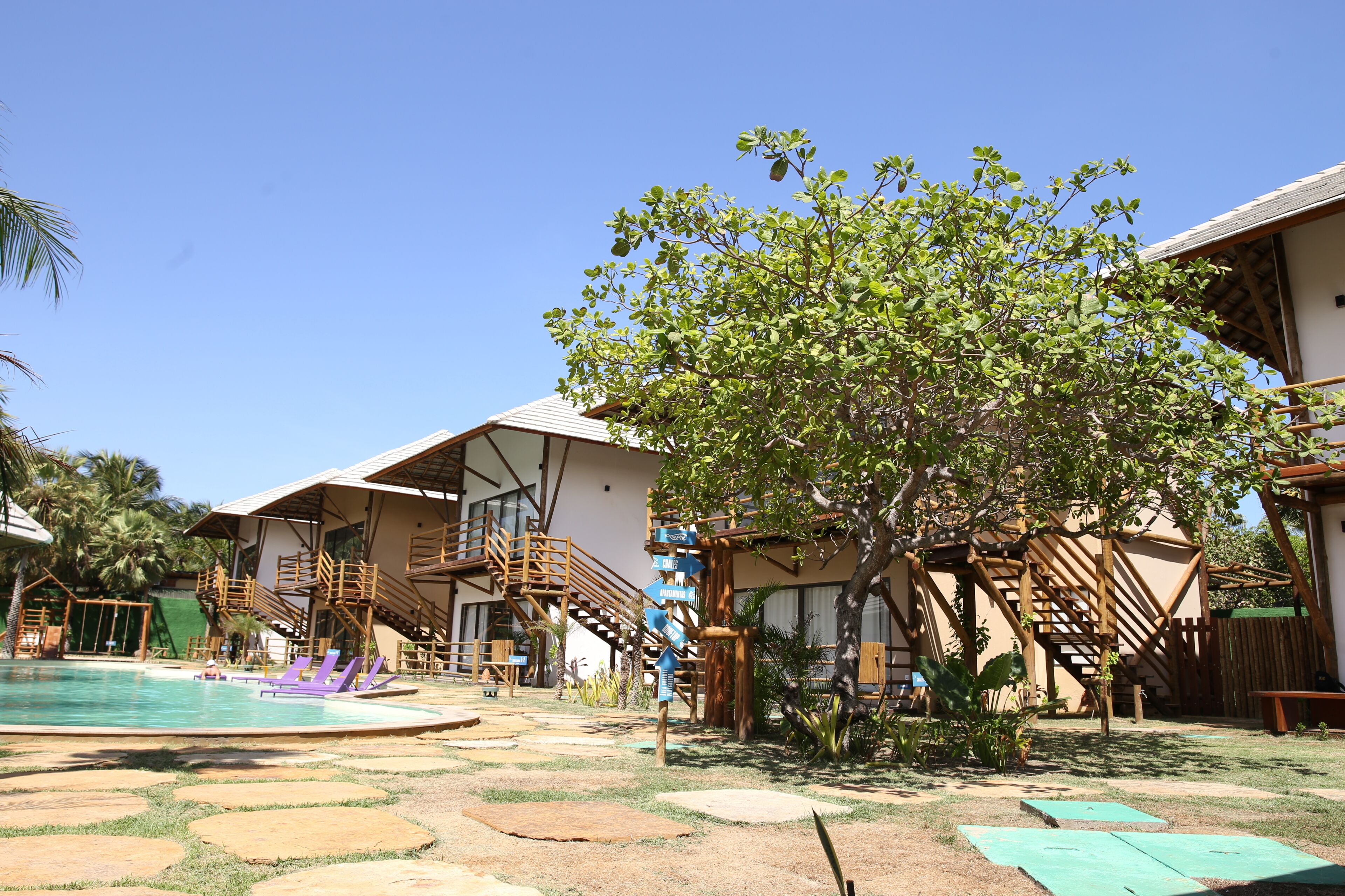 Ein Poolbereich mit Holzdeck und Liegestühlen, umgeben von Gebäuden mit Holztreppen und einem Baum.