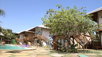 Ein Poolbereich mit Holzdeck und Liegestühlen, umgeben von Gebäuden mit Holztreppen und einem Baum.