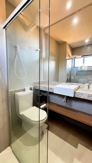Un baño moderno con ducha envuelta en vidrio, inodoro y tocador con lavabo y espejo.