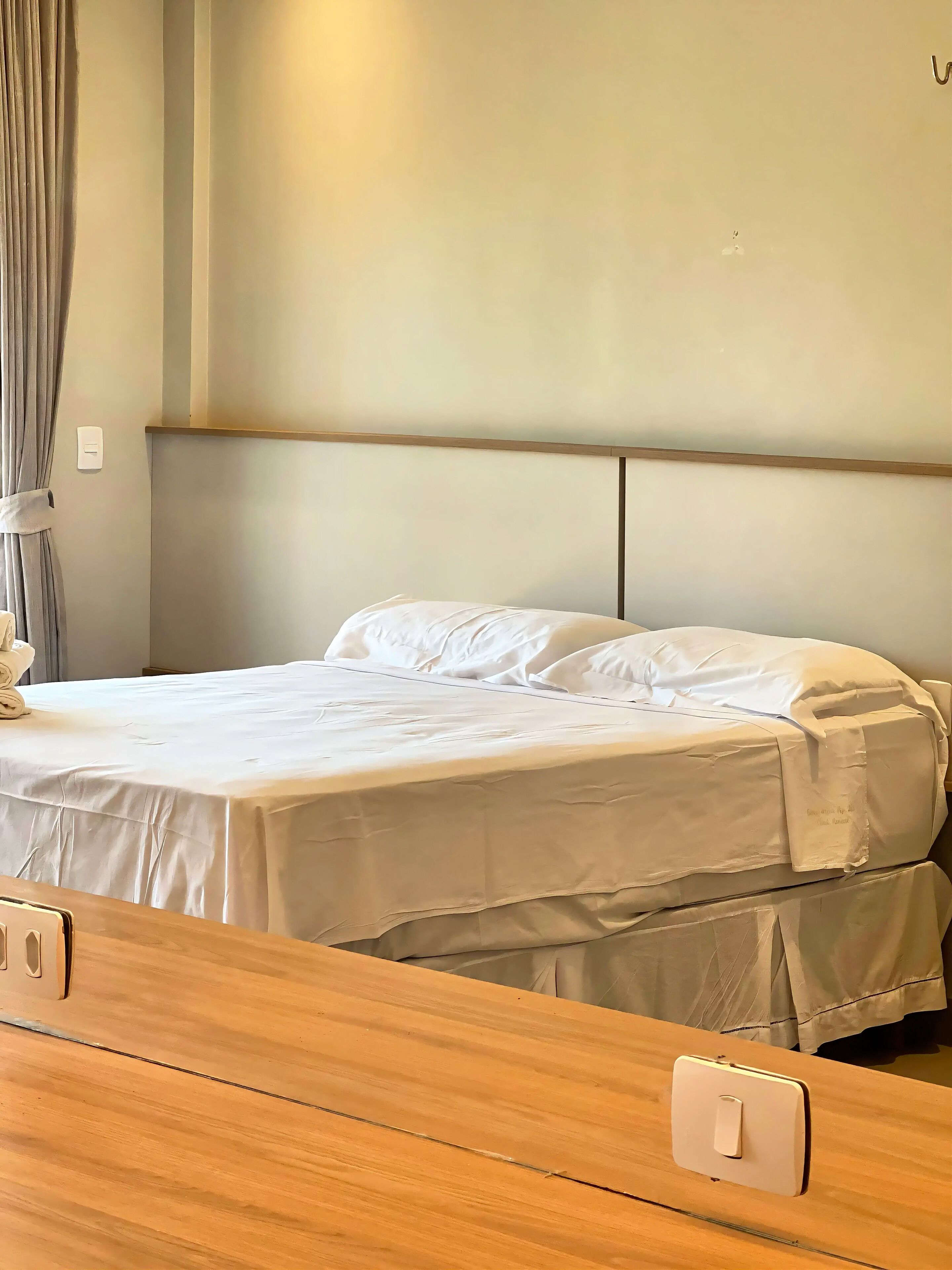 A bed with a wooden headboard, a white bedspread, and a bedside table with a light switch.