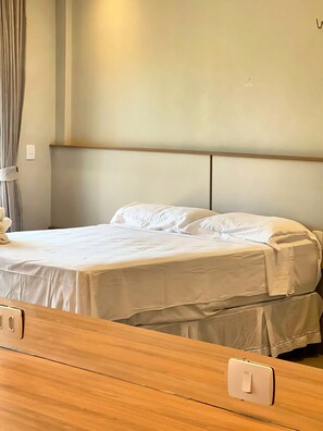 Una cama con cabecera de madera, una colcha blanca y una mesita de noche con interruptor de luz.