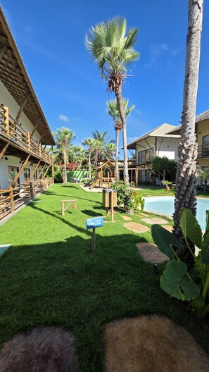 A resort with a swimming pool, palm trees, and a children's play area.