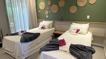 A hotel room with two beds, a green wall with woven art, and a window with curtains.