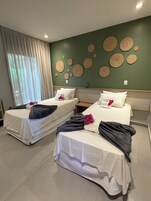 Habitación de hotel con dos camas, una pared verde con arte tejido y una ventana con cortinas.