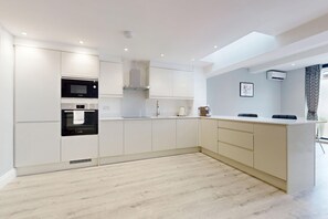 A modern kitchen with white cabinetry, a Bosch microwave, and a built-in oven. - Tidy 1BR Flat w/Parking & Aircon Near River Thames (London)