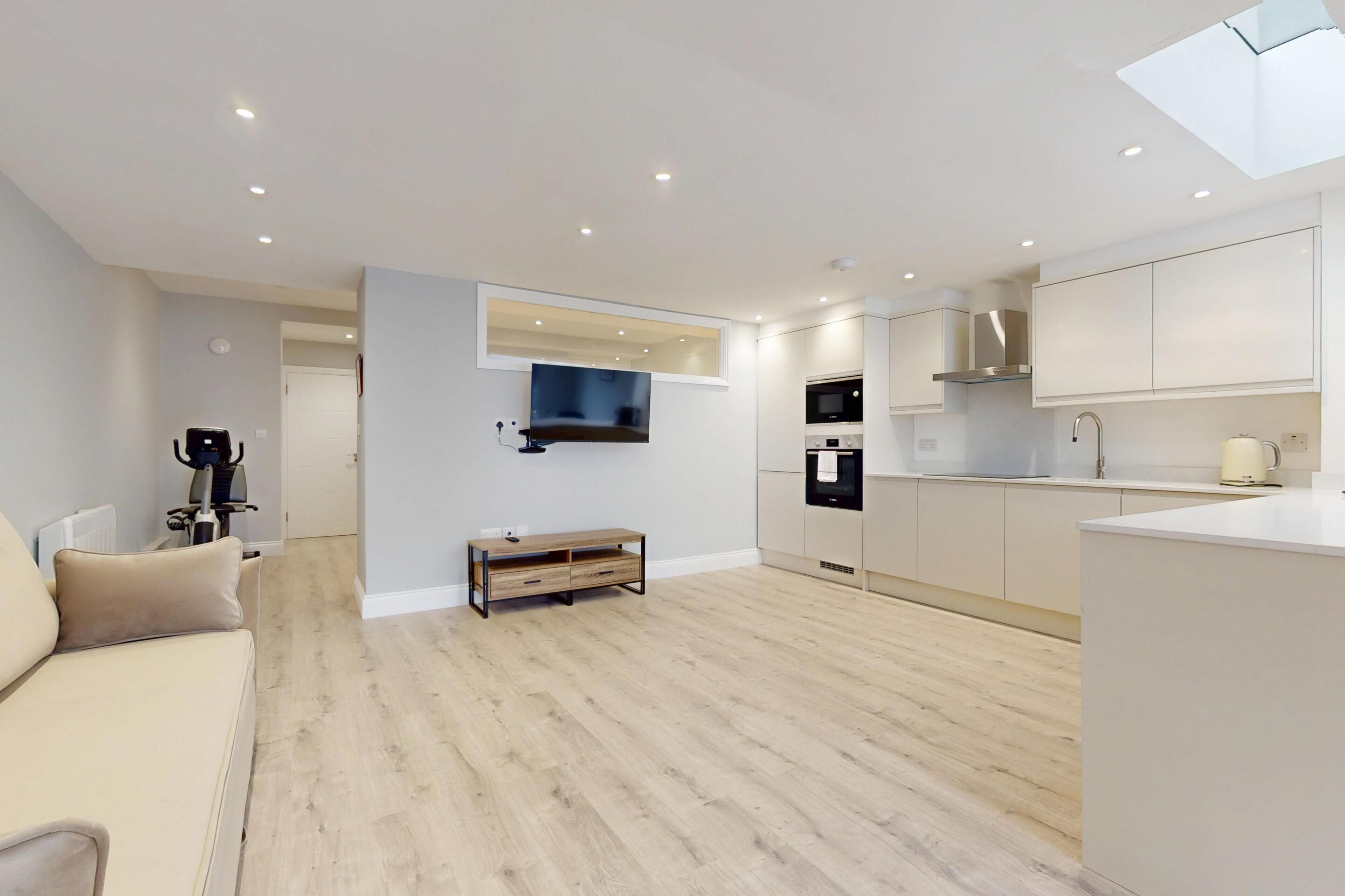 A modern apartment with a living area, kitchenette, and a flat-screen TV mounted on the wall.