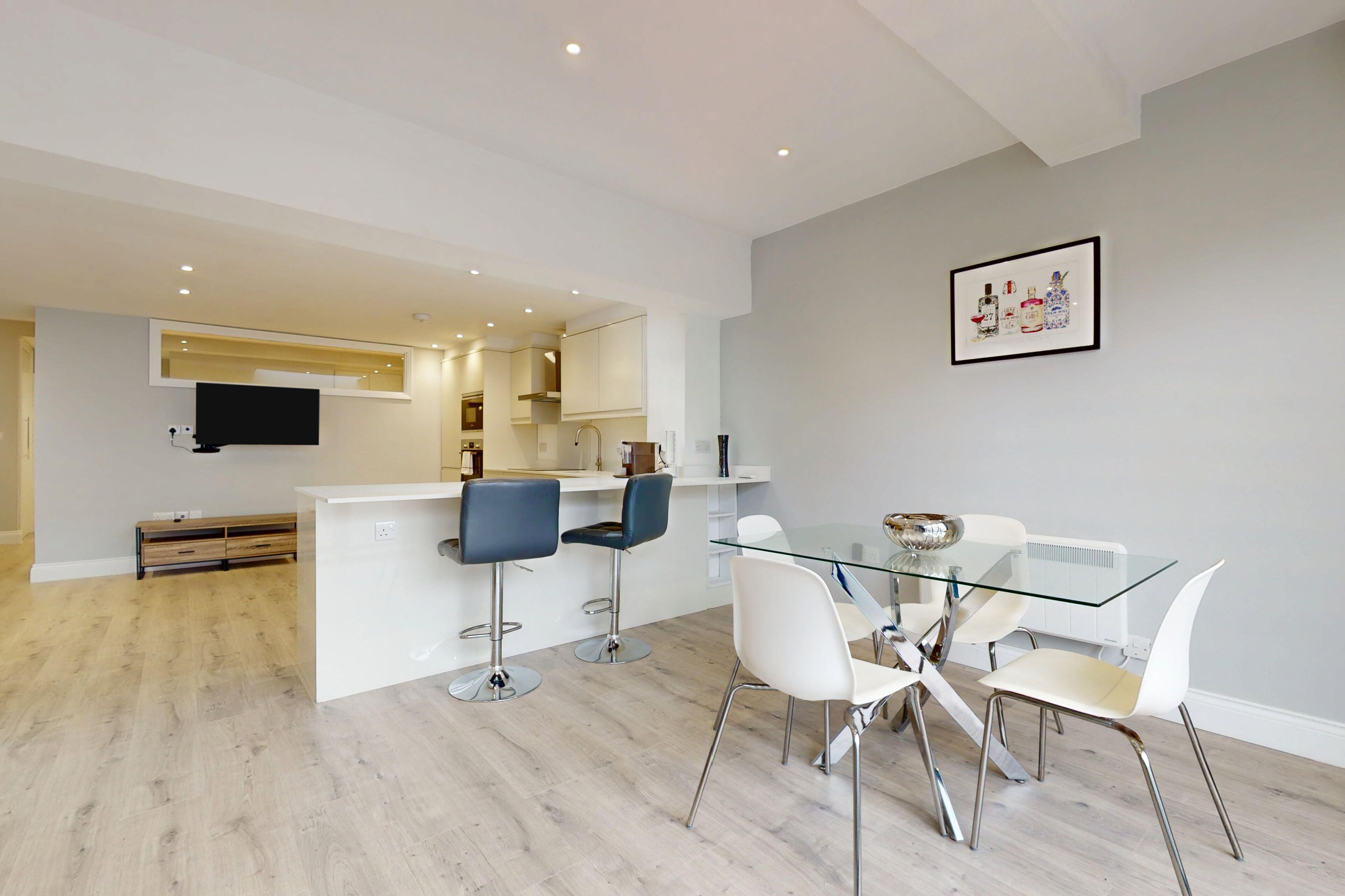 Une cuisine moderne avec des meubles blancs, un îlot central et des tabourets de bar.