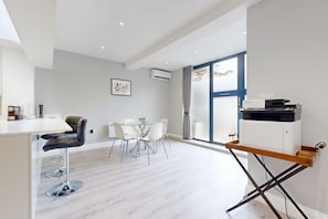 A modern kitchen with a dining area, a large window, and a printer on a stand. - Tidy 1BR Flat w/Parking & Aircon Near River Thames (London)