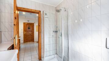 Un baño moderno con cabina de ducha de vidrio, puerta de madera y suelo de baldosas blancas.