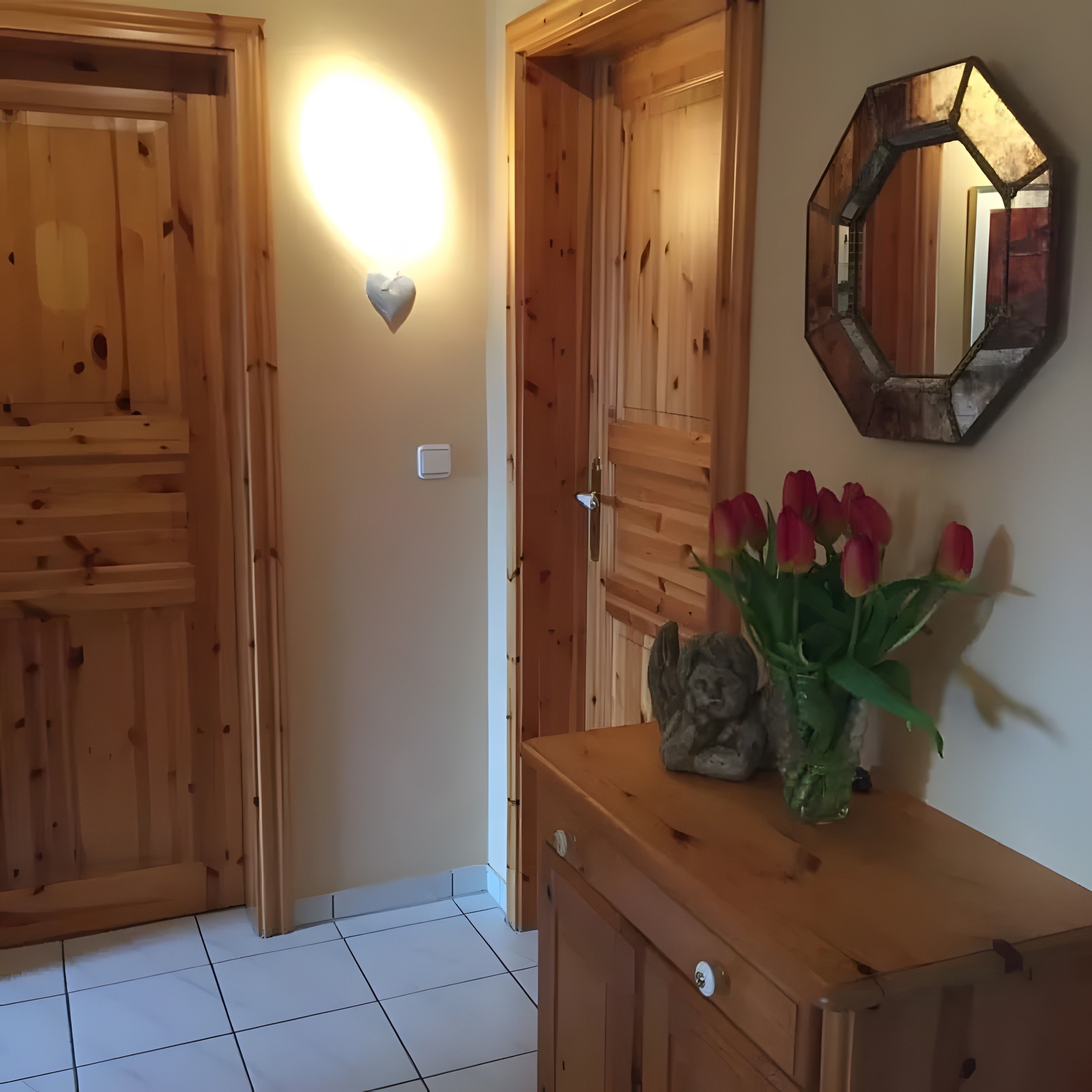 Un interior de madera con una lámpara de pared, un espejo y un florero con flores.