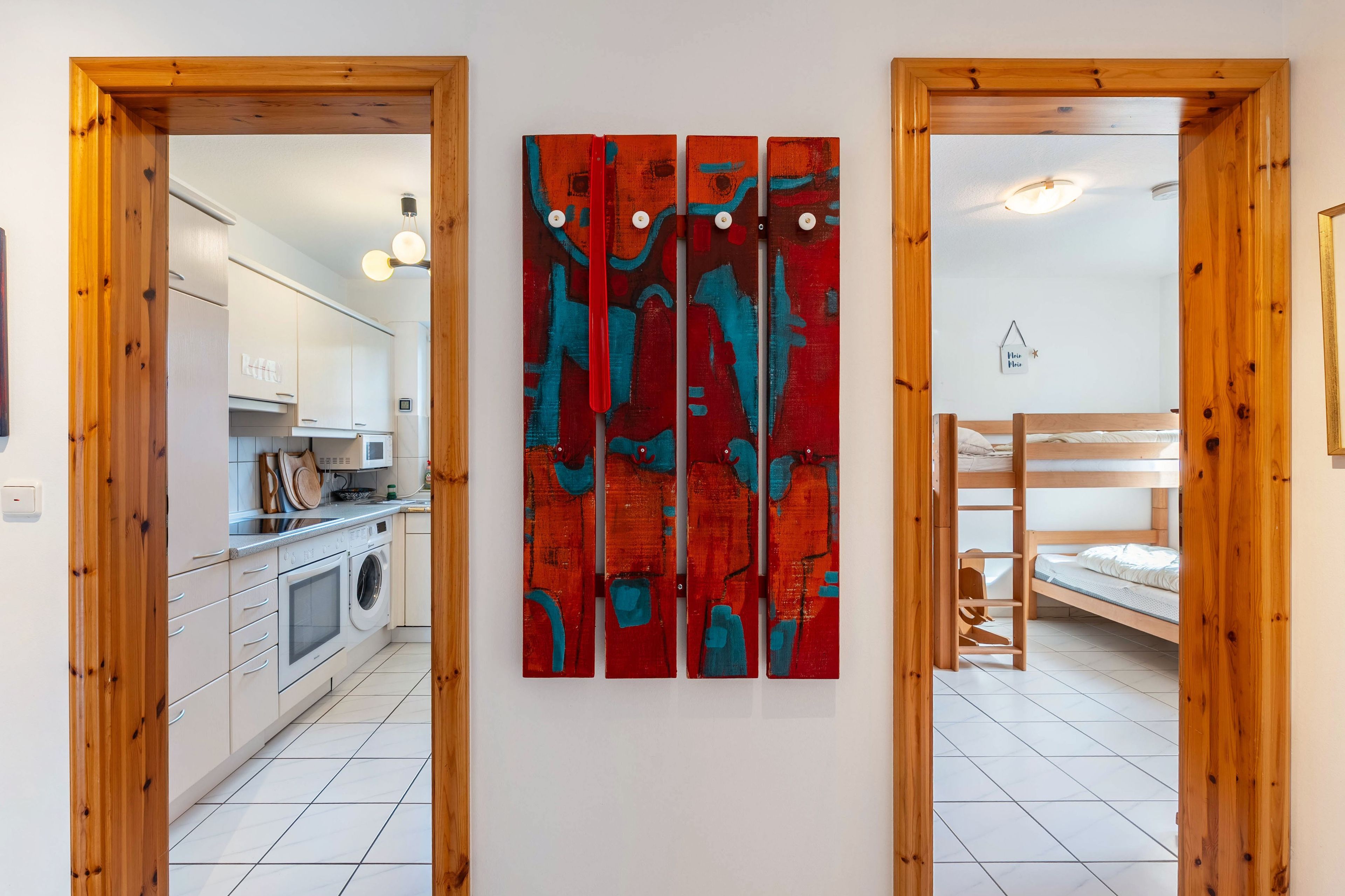 Una habitación con cocina, una litera y una pared con un cuadro abstracto rojo.
