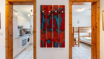 Una habitación con cocina, una litera y una pared con un cuadro abstracto rojo.