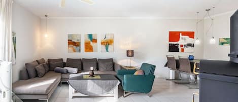 A modern living room with a sofa, armchair, coffee table, and a dining area with chairs.