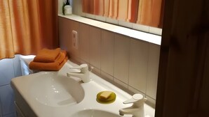 Un bany amb un lavabo blanc, dues aixetes, un mirall i un escurapins amb tovalloles doblegades.