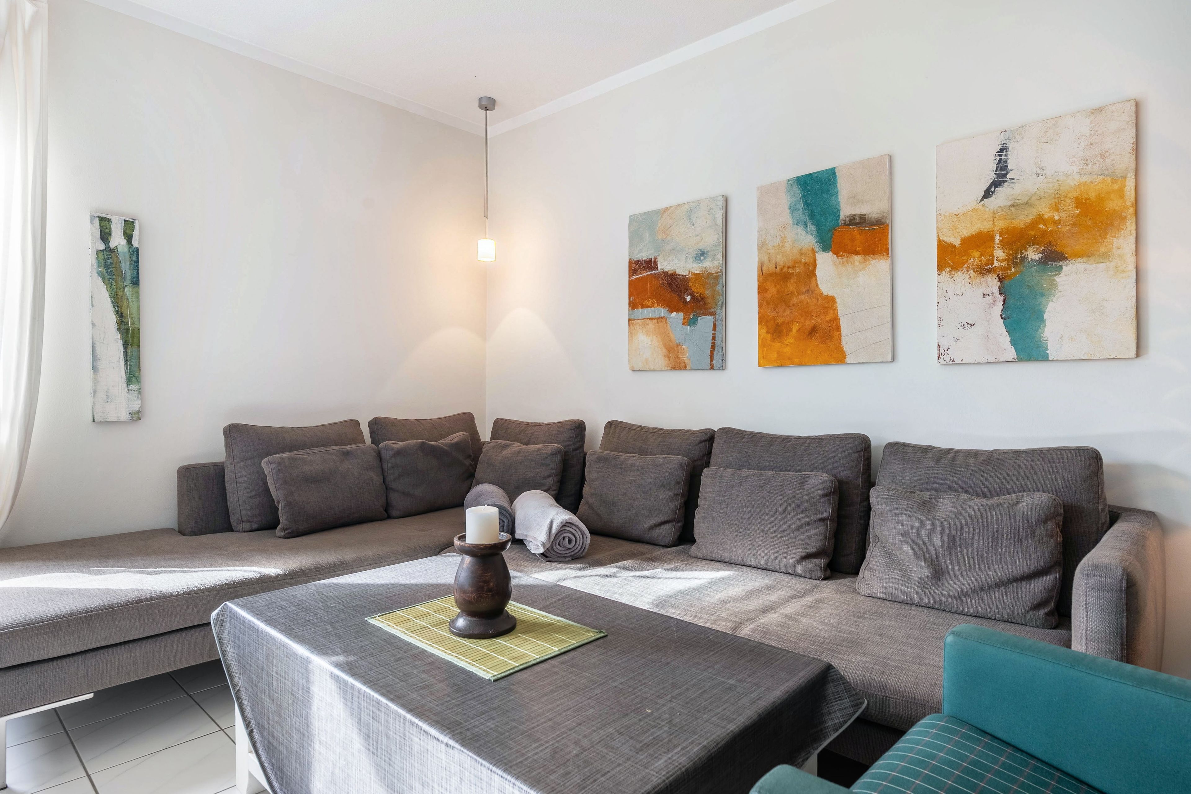 A modern living room with a sofa, a table with a candle, and abstract wall art.
