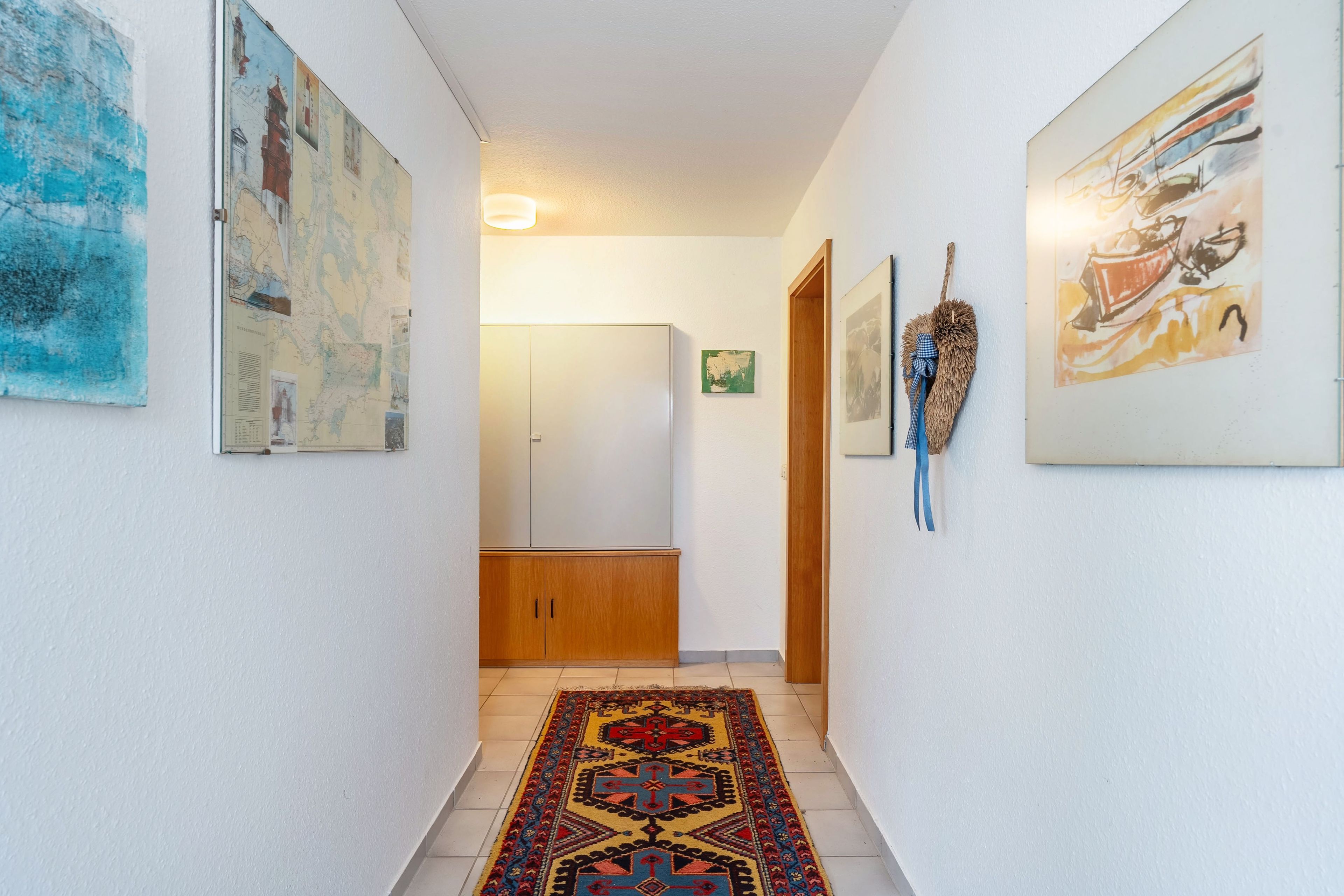 Ein Flur mit Teppichmuster, Holztüren und verschiedenen Kunstwerken an den Wänden.