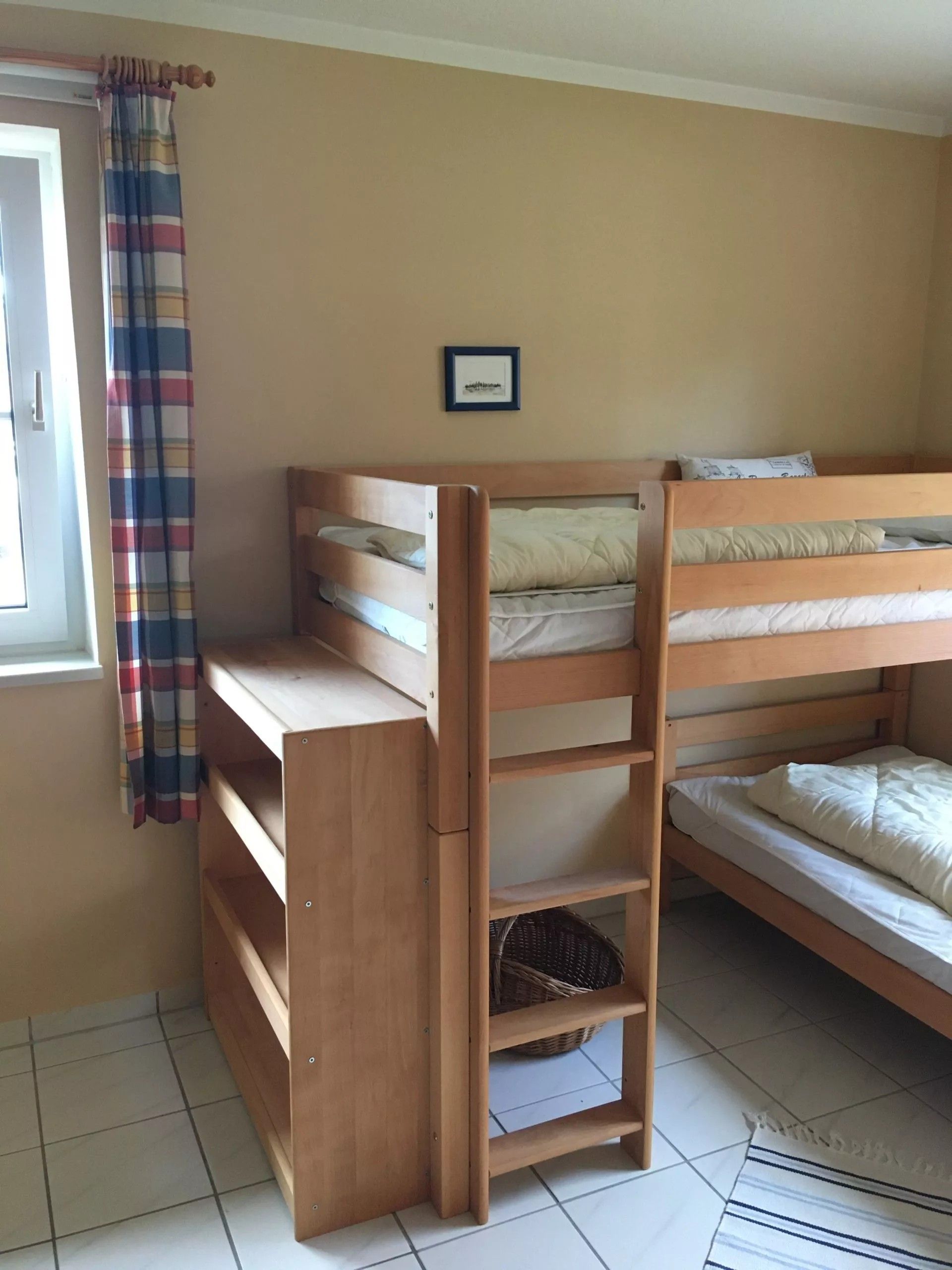 Una cama individual superpuesta con un escritorio debajo, una ventana con cortina y un cuadro en la pared.