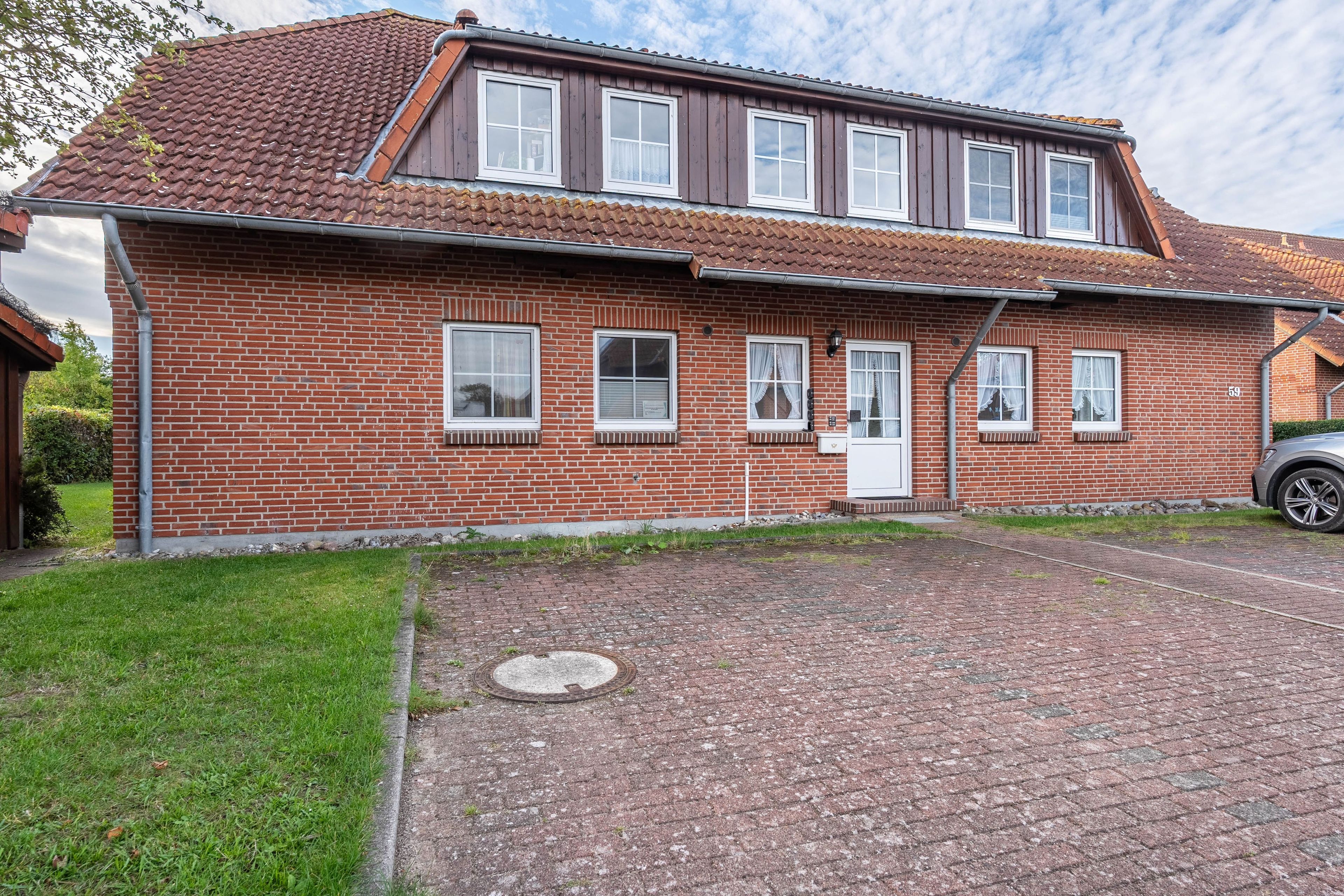 Ein zweigeschossiges Backsteinhhaus mit einem Ziegeldach, einer Veranda und einem gepflasterten Einfahrt.