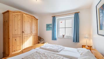 Une chambre avec une armoire en bois, un lit avec une literie blanche, une fenêtre avec des rideaux bleus et une table de chevet avec une lampe.
