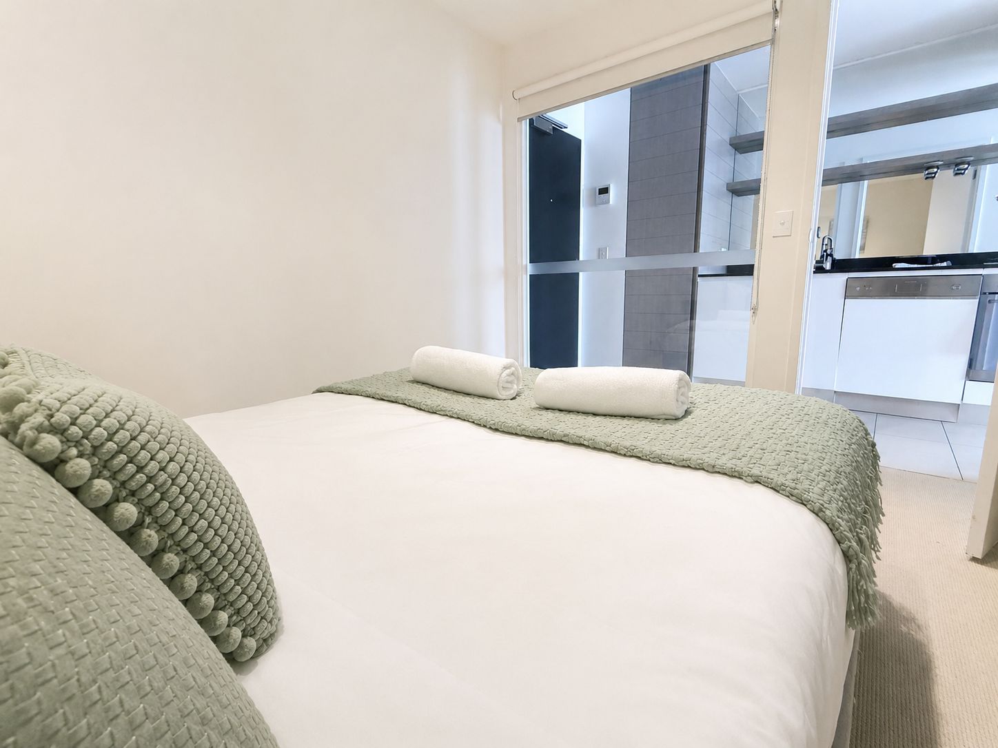 A hotel room with a bed, a green textured throw blanket, and a white towel.