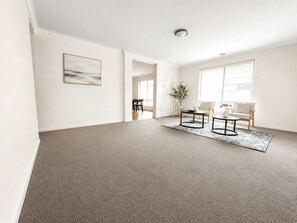 A spacious living room with a neutral color palette, a large window, and a minimalist design. - Elegant Lakeside Escape | Spacious 4BR Home Parkin (Point cook)