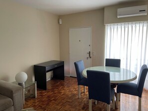 A room with a round glass table, four chairs, a black desk, a sofa, a door, and an air conditioning unit. - Los Arcos Palermo Palace (Buenos Aires)