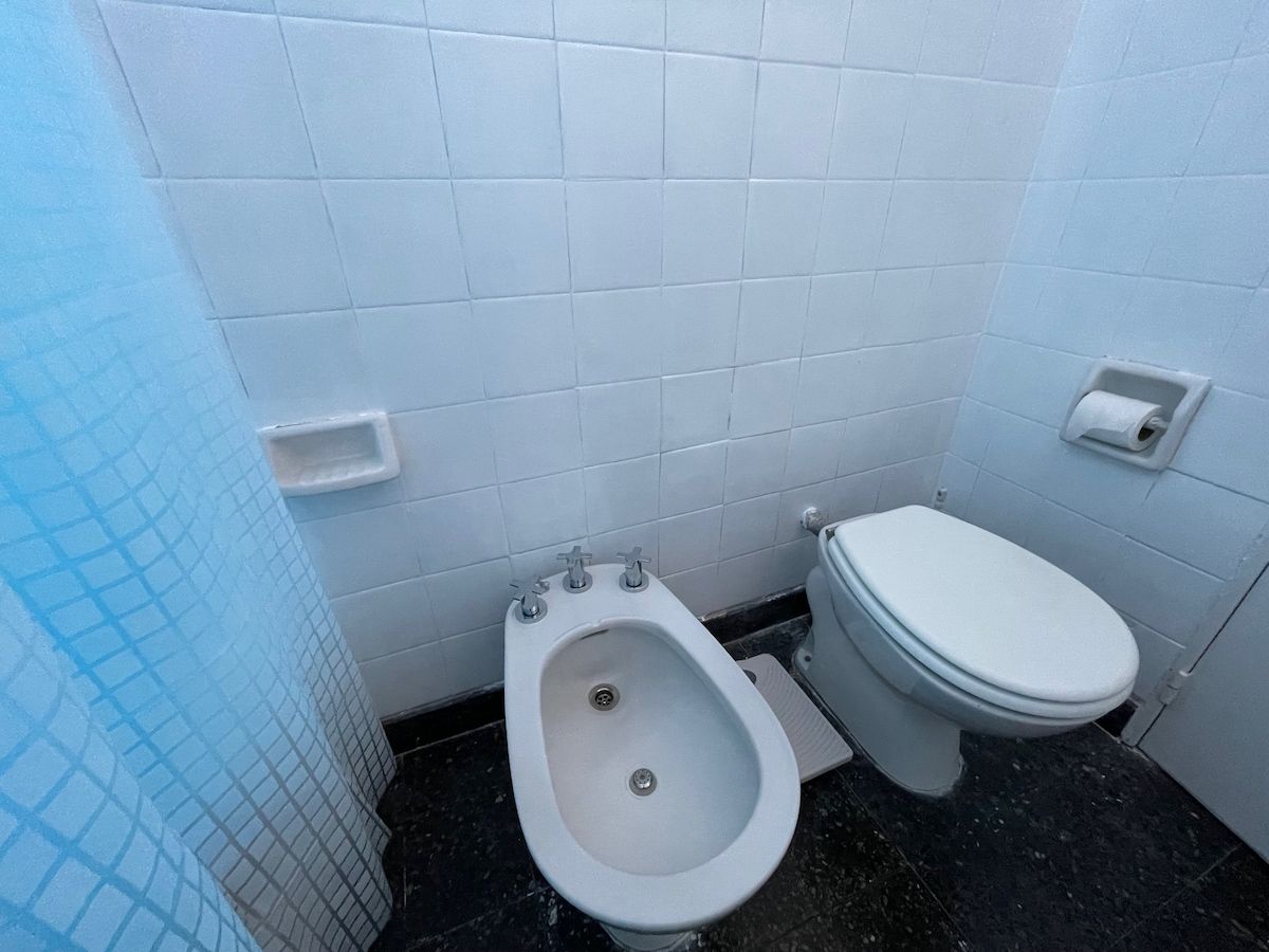 A bathroom with a bidet, toilet, and a hand dryer.