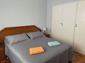 A single bed with a grey bedspread, two pillows, a wooden headboard, a nightstand with a lamp, and a wardrobe with two doors. - Los Arcos Palermo Palace (Buenos Aires)