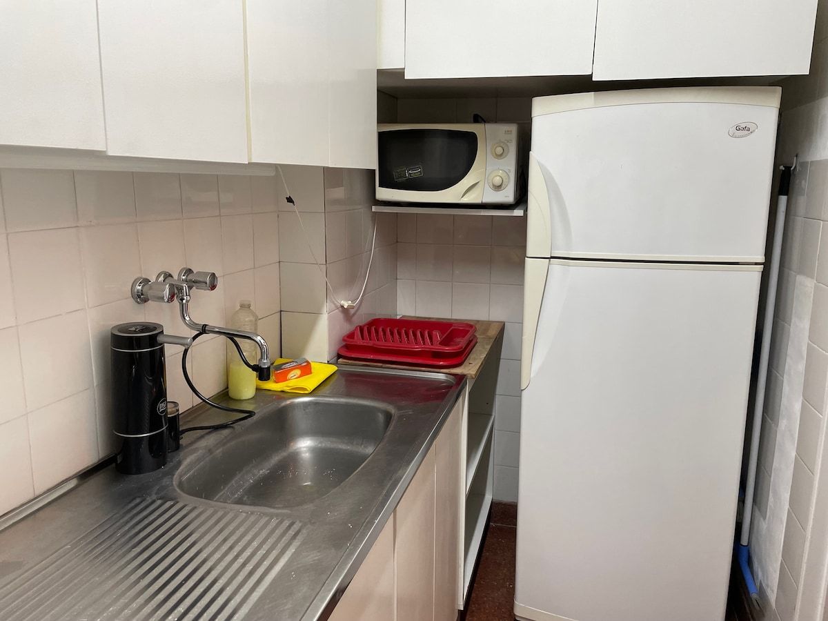 A compact kitchen with a stainless steel sink, a microwave, and a white refrigerator.