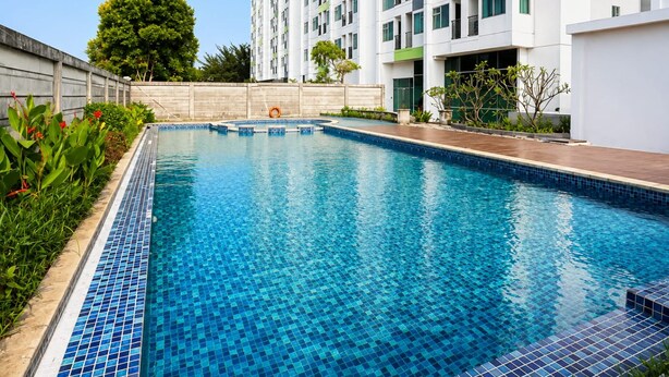 A rectangular swimming pool with blue mosaic tiles, surrounded by a wooden deck and a low brick wall. - Starla Room Enviro Cikarang by BukaKamar (Cikarang/Bekasi)