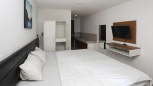 A hotel room with a bed, a TV mounted on the wall, and a small desk area. - Starla Room Enviro Cikarang by BukaKamar (Cikarang/Bekasi)