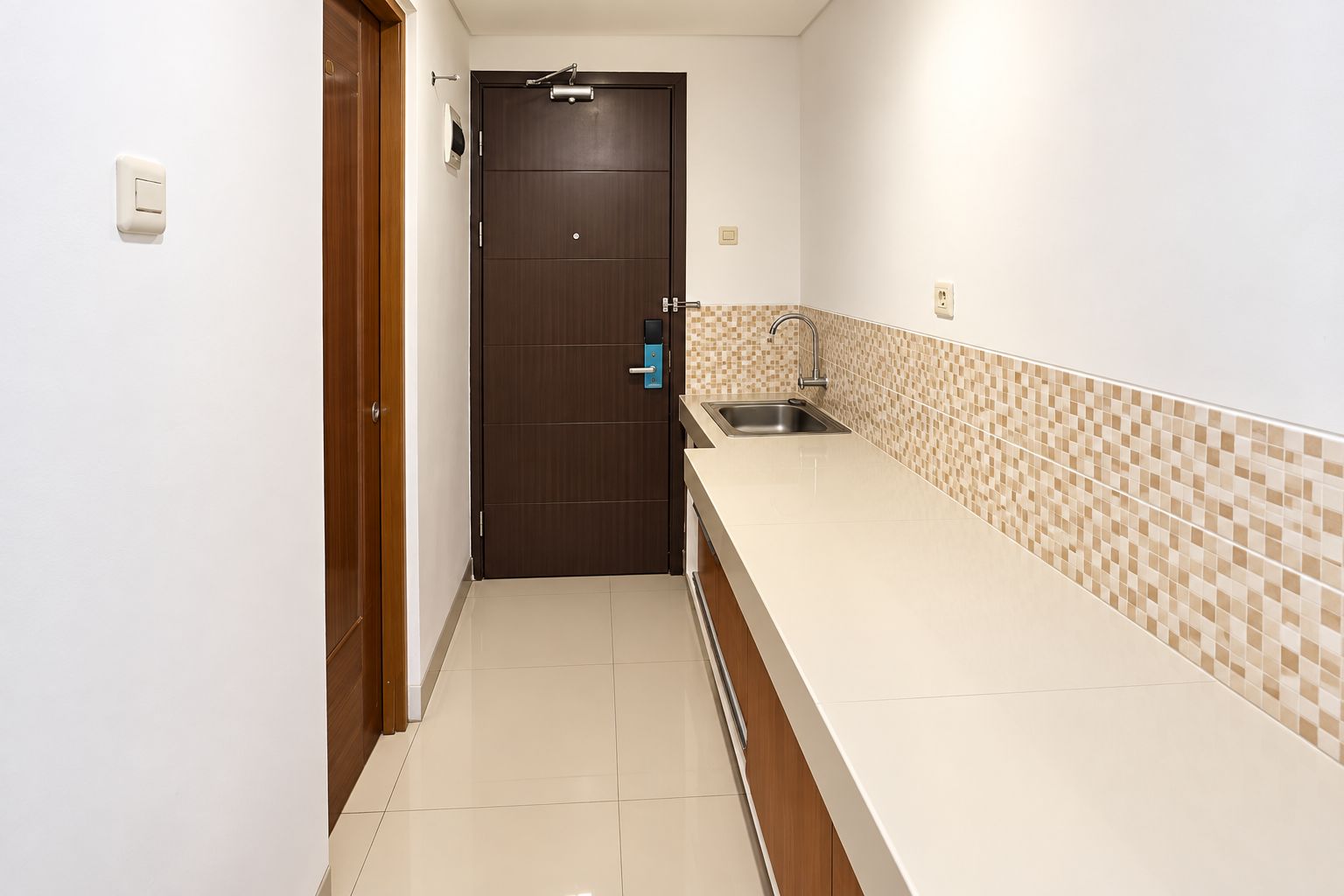 Una cocina estrecha con salpicadero de azulejos, un lavamanos de acero inoxidable y una puerta de madera.